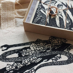 A close up shot of a gold Baby Vamp necklace with a snake and crystal printed tote in the foreground