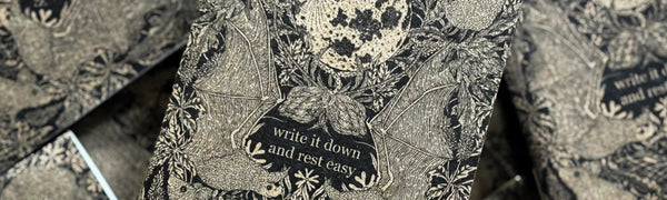 A multitude of Fennec Design pocket notebooks lay in a pile, each adorned with botanical and organic elements and the words "write it down and rest easy"