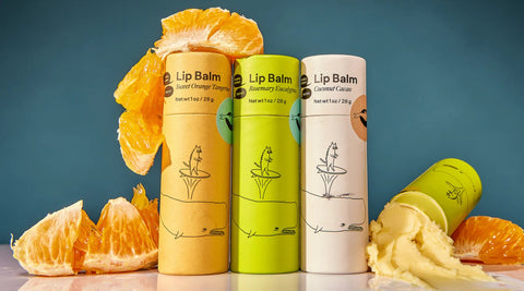 Meow Meow Tweet lip balms in orange, cream, and green tubes are displayed next to orange peels