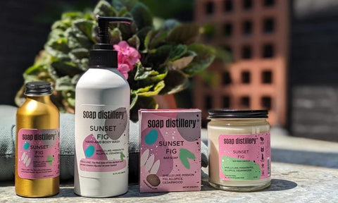 Sunset Fig scented Soap Distillery products in purple packaging sit in the sun